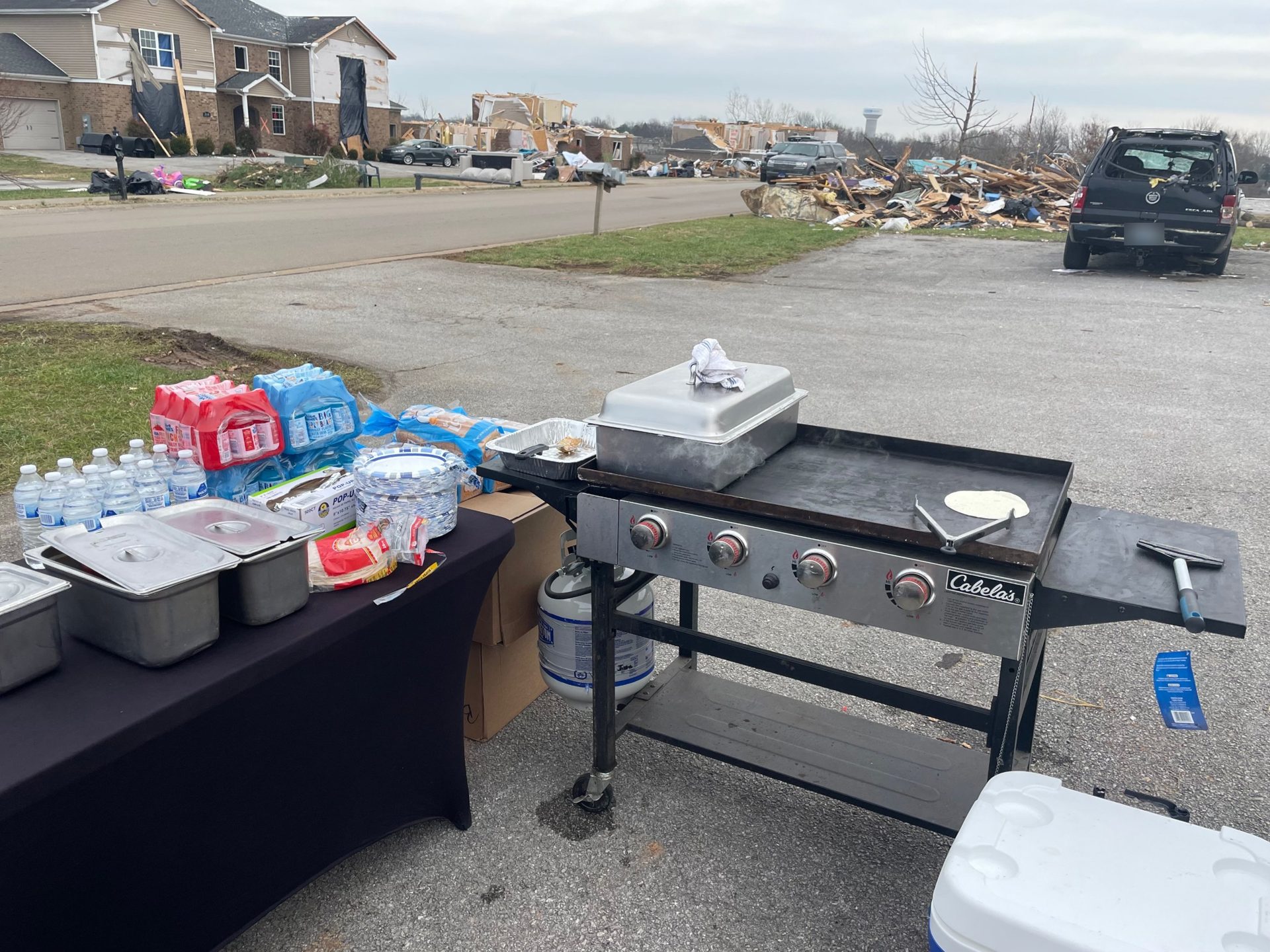 Griddle and supply table set up on a street with storm-damaged homes behind