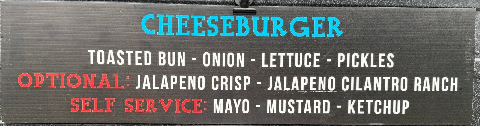 Menu sign: Cheeseburger — toasted bun, onion, lettuce, pickles; optional jalapeño crisp and jalapeño cilantro ranch; self-serve mayo, mustard, ketchup
