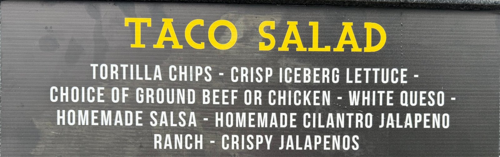 Menu sign: Taco Salad — tortilla chips, crisp iceberg lettuce, choice of ground beef or chicken, white queso, homemade salsa, homemade cilantro jalapeño ranch, crispy jalapeños
